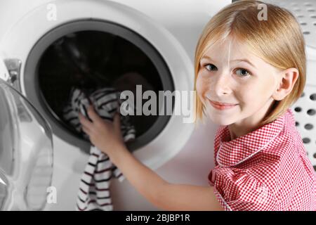 Small girl putting cloth into washing machine Stock Photo