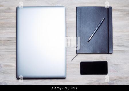 minimalist flat lay of a laptop, smart phone, notebook and pen on a wooden table, concept of online entrepreneur and remote work Stock Photo