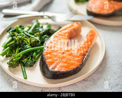 Ready-to-eat grilled salmon steak and greens - baby broccoli or broccolini and spinach on rustic craft plate over gray background. Keto diet dish. Stock Photo