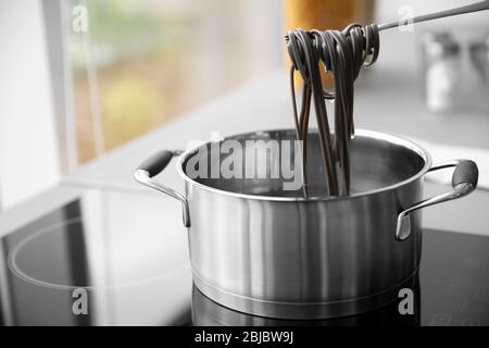 Black pasta on fork over pan in kitchen Stock Photo