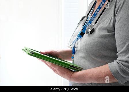 senior female doctor holding computer tablet with stethoscope and nhs lanyard around neck Stock Photo