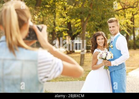 Young woman taking photo of happy wedding couple in park Stock Photo