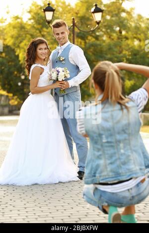 Young woman taking photo of happy wedding couple in park Stock Photo