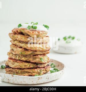 Zucchini fritters. Traditional zucchini fritters in stack on white background. Zucchini pancakes or fritters with green onion and parmesan cheese,served sour cream or greek yogurt. Copy space for text Stock Photo