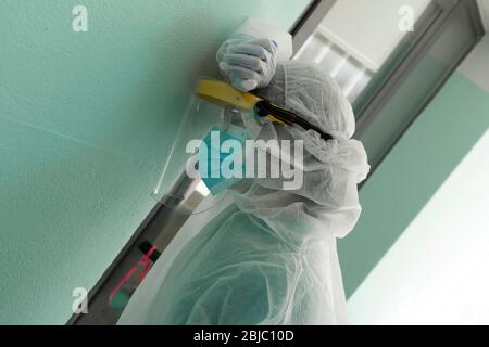 Tired and stressed nurse with uniform and mask and gown to protect herself from the infection leaning desperately against the hospital wall Stock Photo