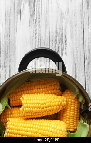 Tasty boiled corncobs in saucepan on wooden table Stock Photo