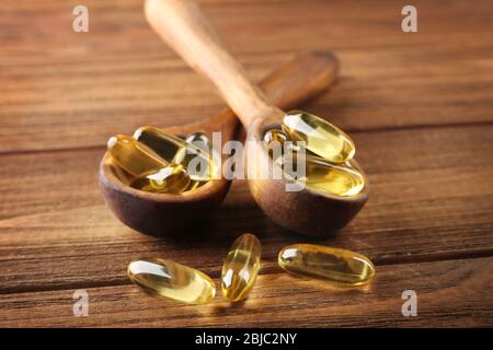 Cod liver oil capsules in spoons on wooden background Stock Photo