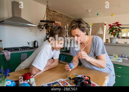 mother and son colouring Easter egg at home in the kitchen Stock Photo