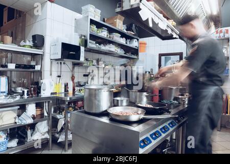 Behind the scenes of brands. The chef cooking in a professional kitchen of a restaurant meal for client or delivery. Open business from the inside. Meals during the quarantine. Hurrying up, motion. Stock Photo