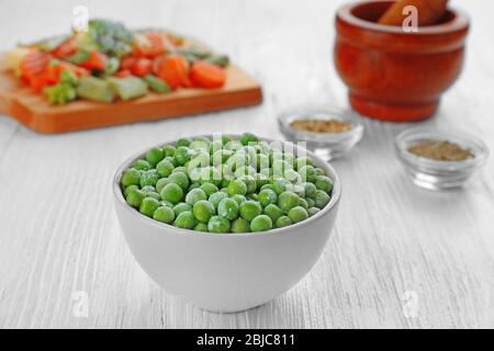 Frozen peas in bowl on wooden background Stock Photo