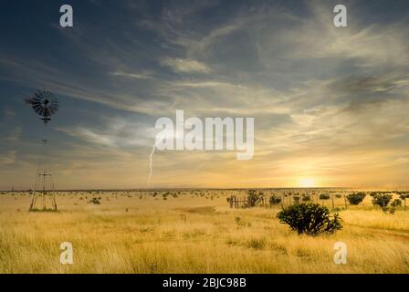 Windmill in a Texas field along Route 66 with a storm approaching and lightening in the distance Stock Photo