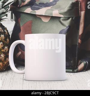 White Mug Mockup, in front of a army fabric backpack. Perfect for businesses selling mugs, just overlay your quote or design on to the image. Stock Photo