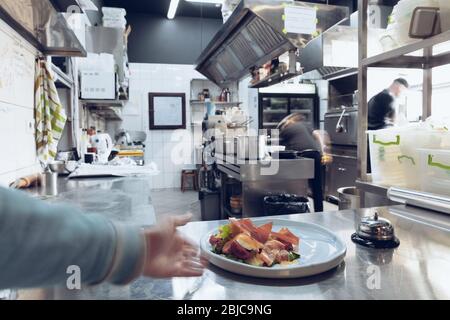 Behind the scenes of brands. The chef cooking in a professional kitchen of a restaurant meal for client or delivery. Open business from the inside. Meals during the quarantine. Hurrying up, motion. Stock Photo