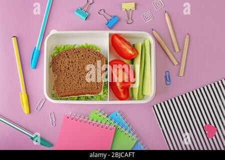 Lunchbox with dinner and stationery on pink background Stock Photo