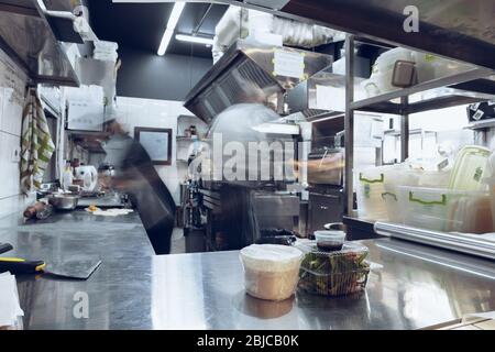 Behind the scenes of brands. The chef cooking in a professional kitchen of a restaurant meal for client or delivery. Open business from the inside. Meals during the quarantine. Hurrying up, motion. Stock Photo