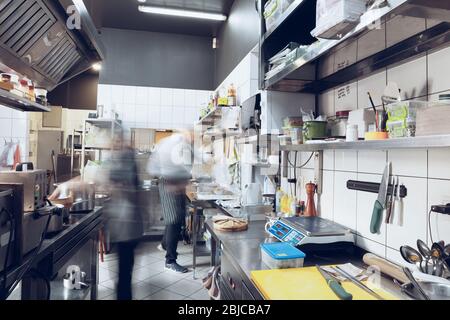 Behind the scenes of brands. The chef cooking in a professional kitchen of a restaurant meal for client or delivery. Open business from the inside. Meals during the quarantine. Hurrying up, motion. Stock Photo