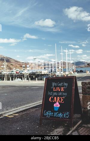 'You can't buy love, but you can buy cake' announcement written on a chalk blackboard, attracting customers to the local cafe in Ullapool village in S Stock Photo