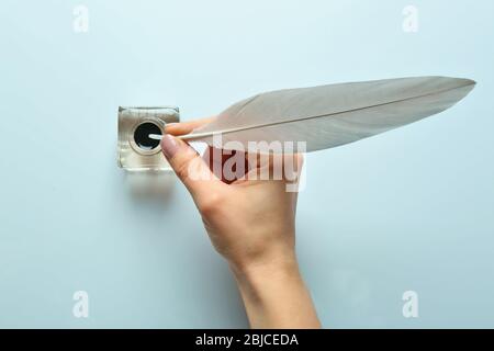 Female hand dipping feather pen into inkwell on light background Stock Photo