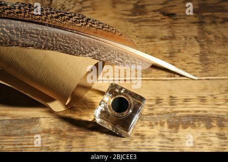Feather pen with inkwell and scroll on wooden background Stock Photo