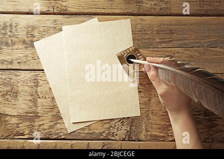 Female hand writing with feather pen and inkwell on wooden background Stock Photo