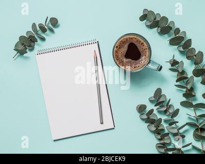 Blank paper notebook with pencil and coffee cup. Empty paper sketchbook with pincil and eucalyptus branches on blue background. Top view or flat lay. Copy space for text or design. Stock Photo