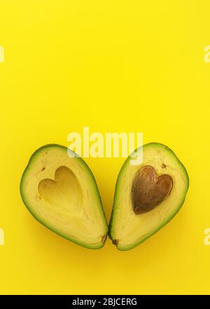 Flat lay of cut in half avocado with seed in shape of heart on yellow background love forever inseparable concept Stock Photo