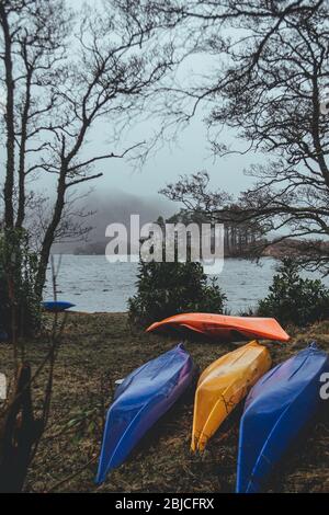 Colorful modern kayaks lying upside down on the shore of a lake in Scotland on a cloudy rainy day Stock Photo