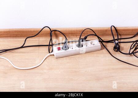 Plug strip with a red on off switch on the floor, white power extension cord plugs connected to it, tangled black wires, european plugs, empty room Stock Photo