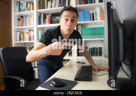 Seated man in black shirt looking at the computer screen very surprised. Mid shot. Stock Photo