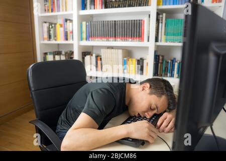 Seated man in black shirt asleep on the computer keyboard. Mid shot. Stock Photo