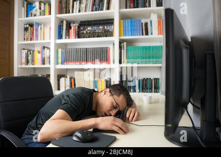 Seated man in black shirt asleep on the computer keyboard. Mid shot. Stock Photo