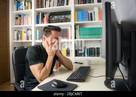 Seated man in a black shirt in front of the computer, hysterical because he does not understand something. Mid shot. Stock Photo
