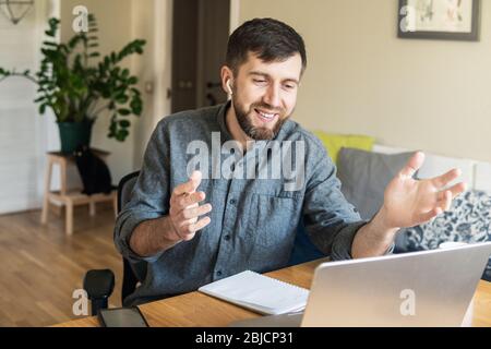 Handsome Eastern European man working from home during Corona virus quarantine lockdown, having online video chat with his colleagues Stock Photo