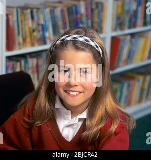Schoolgirl pupil student in uniform 8-10 years attractive confident happy portrait in school library with books behind junior school interior facility Stock Photo