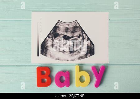 Colourful word BABY and ultrasound photo on blue wooden background Stock Photo