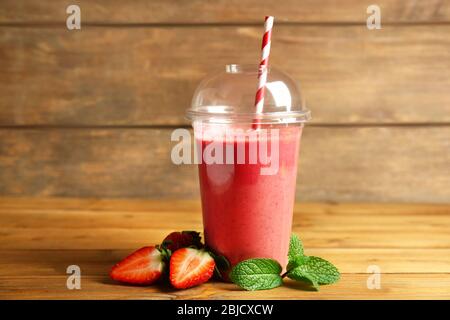 Delicious strawberry milkshake in plastic cup on wooden background Stock Photo