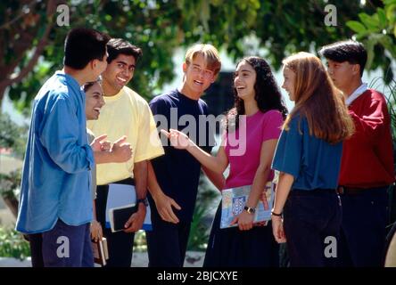 School students multicultural group of 7 happy attractive teenage senior school college high school multicultural students in colourful t shirts relaxing talking and interacting outside in a sunny school college campus environment Stock Photo