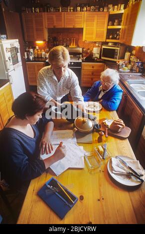 Three female women generations at home living together, with elderly Grandmother, mother and granddaughter together at meal time in their home kitchen, with hard pressed mother serving a meal to table Stock Photo