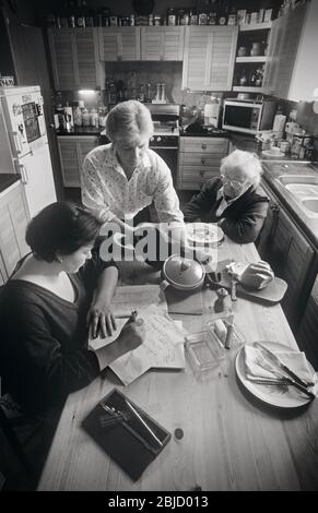 Three generations at home living together, with elderly Grandmother, mother and granddaughter together at meal time in their home kitchen Stock Photo
