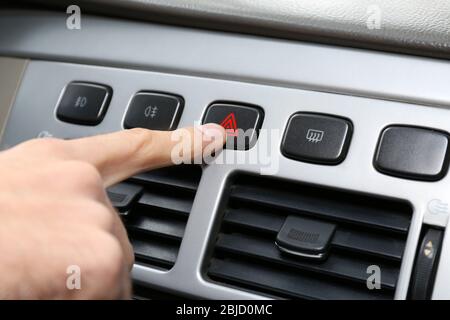 Male hand pressing emergency warning button on car console, closeup Stock Photo