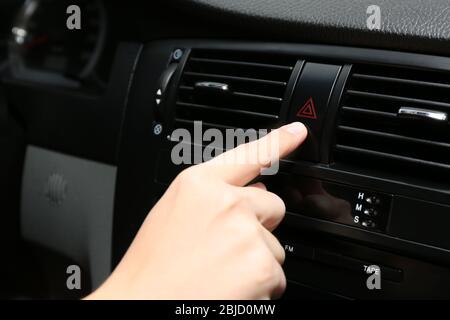 Female hand pressing emergency warning button on car console, closeup Stock Photo