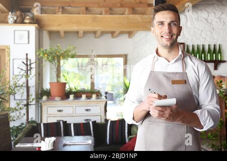 Handsome young waiter with notebook and pen at restaurant Stock Photo