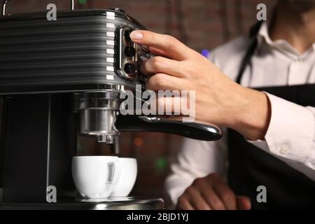 Male barista making fresh espresso in coffee maker, close up Stock Photo