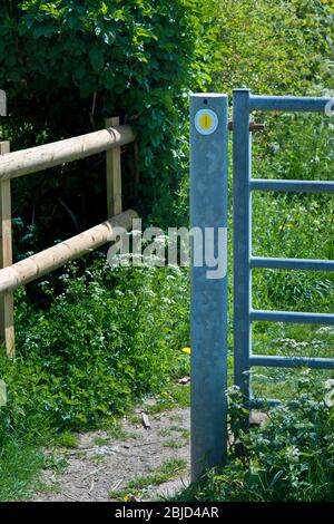 Sign directing walkers past metal gate across road allowing entry on foot only. Stock Photo