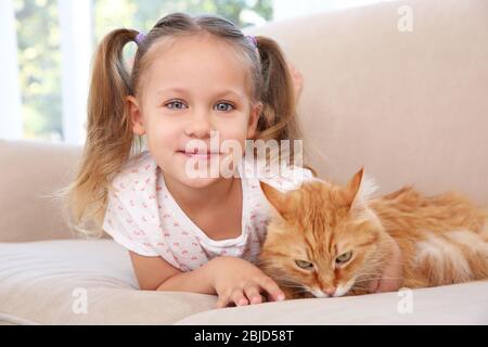 Cute little girl lying on sofa with red cat Stock Photo