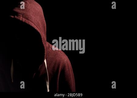 Faceless man in a hoody in dark shadows to disguise face Stock Photo