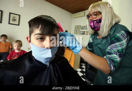 Belgrade, Serbia. 29th Apr 2020. A hairdresser, wearing a protective face mask and protective gloves, cuts the client's hair who also wears a protective face mask. Serbian authorities have decided to ease some of the restrictive measures allowing some businesses to reopen their shops in a move to ease some of the measures that have been in place to limit the spread of coronavirus SARS-CoV-2 which causes the COVID-19 disease. Credit: Koca Sulejmanovic/Alamy Live News Stock Photo