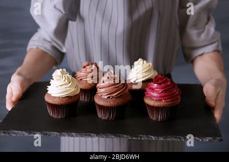 Woman holding slate plate with tasty cupcakes, close up Stock Photo