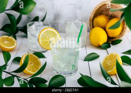 Lemon soda glasses with ice on a table with lemons at an outdoor picnic in nature. Refreshing, healthy, vitamin-rich drinks. Stock Photo