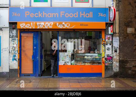 Peckham, UK. 29th April, 2020. A male shop owner talks on his mobile phone outside Peckham Food Hall in South London. ( Credit: Sam Mellish/Alamy Live News ) Stock Photo